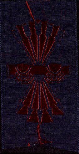 Insignia de tela negra con escudo, con bordado mecánico en rojo del símbolo del yugo y las flechas de Falange.